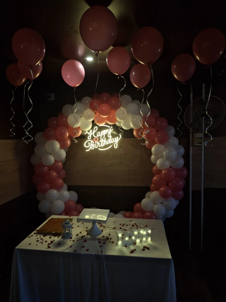 Birthday surprise decoration setup with balloons, floral décor, LED backdrop, candle light arrangement, and personalized celebration by Joyful Knots Events